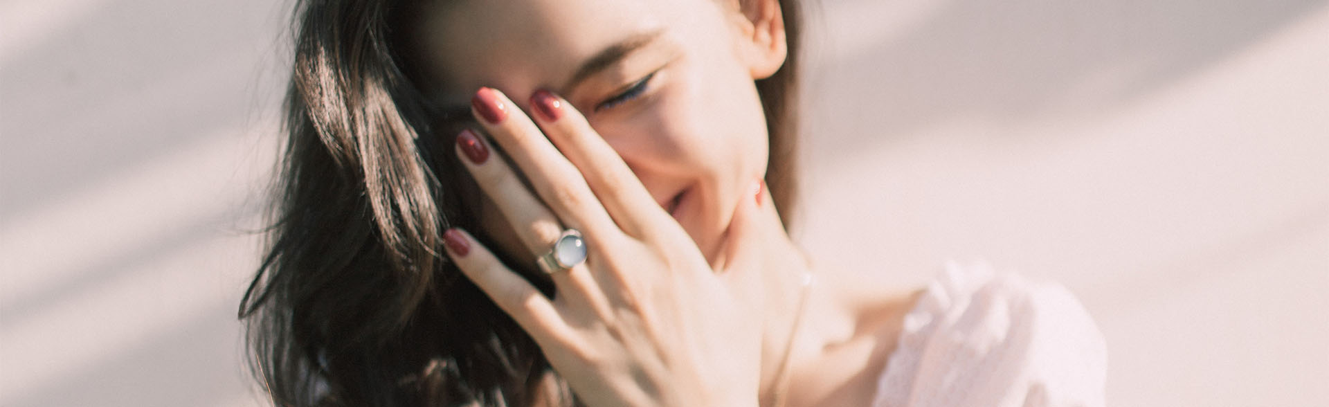 Lachende Frau mit braunen Haaren und weißem Top hält sich die Hand vor den Mund.